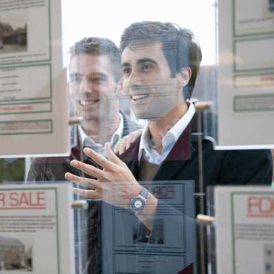 Couple looking at details of home for sale in estate agents window